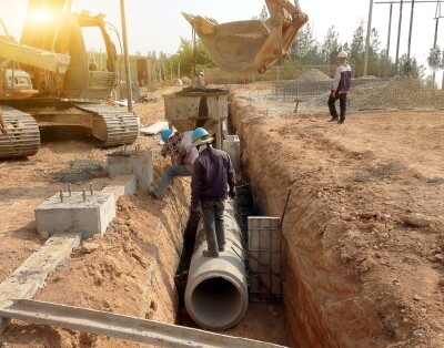 Workers installing drainage pipe along road.