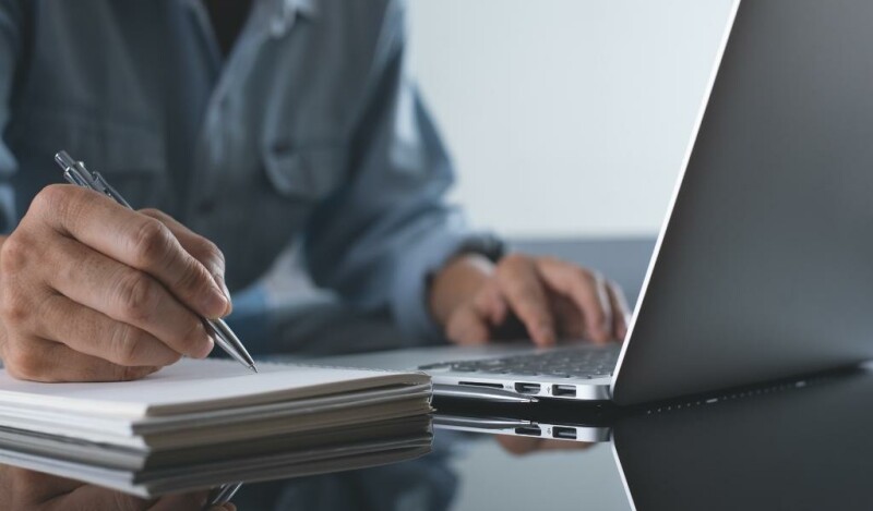 Man working on laptop while taking notes