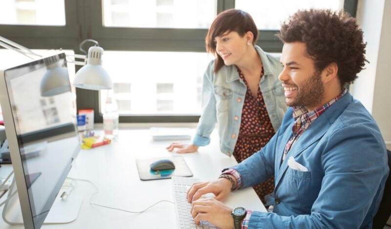Two young trendy coworkers smiling at computer screen