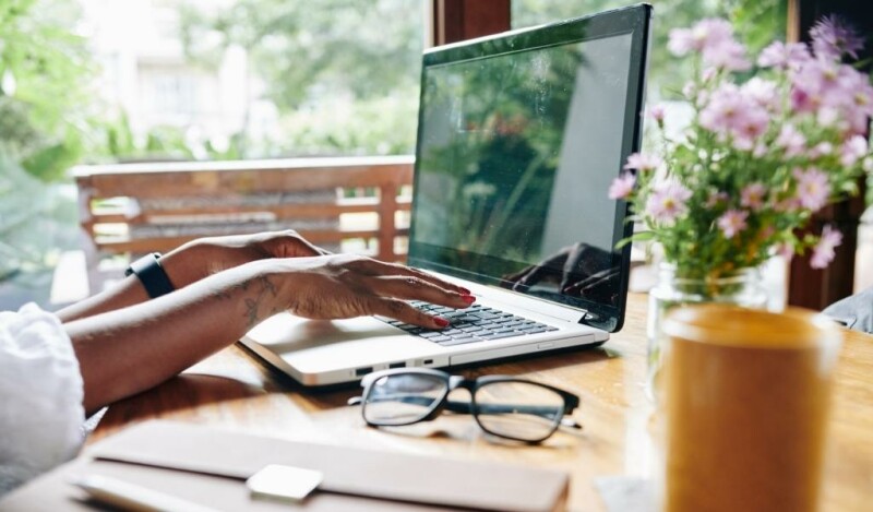Woman with tattoos working at laptop with glasses folded next to her