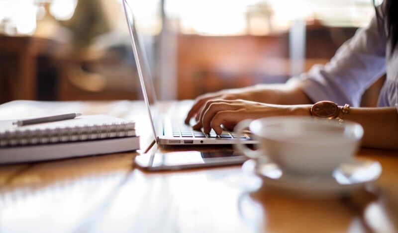Woman working at laptop from a cafe with a cup of coffee or tea next to her