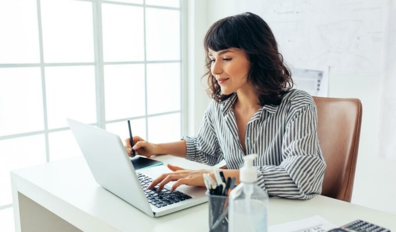 Woman smiling while working on laptop at her desk from home