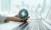 Woman seated at desk holding a small globe above her laptop. Dollar sign icons are overlaid.