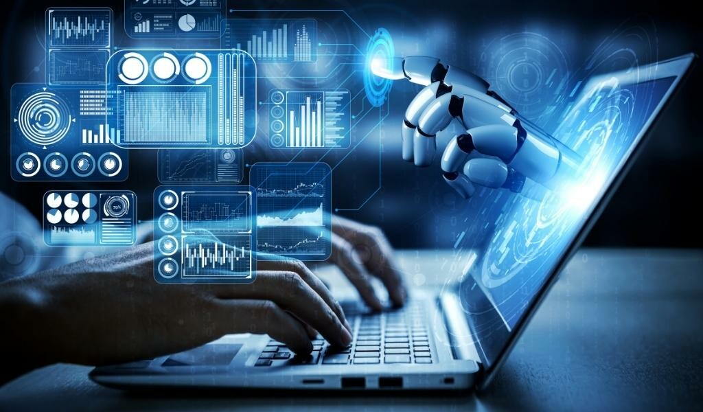 Person working on laptop with artificial intelligence or robot hand reaches out pointing to abstract technology designs