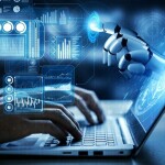 Person working on laptop with artificial intelligence or robot hand reaches out pointing to abstract technology designs