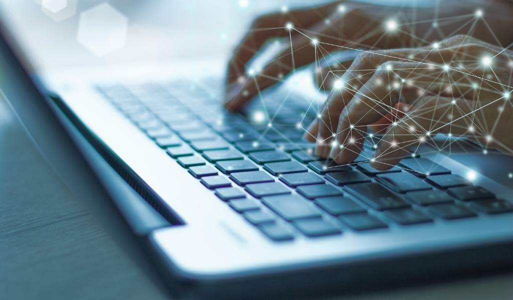 Person working with fingers on their laptop keyboard and abstract lights with lines around it