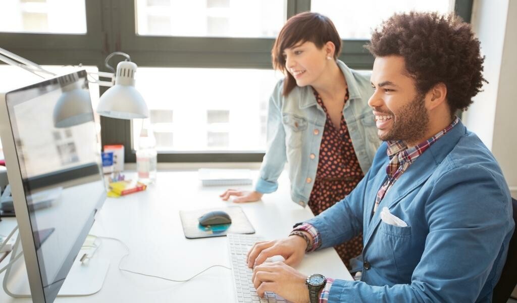Two young trendy coworkers smiling at computer screen