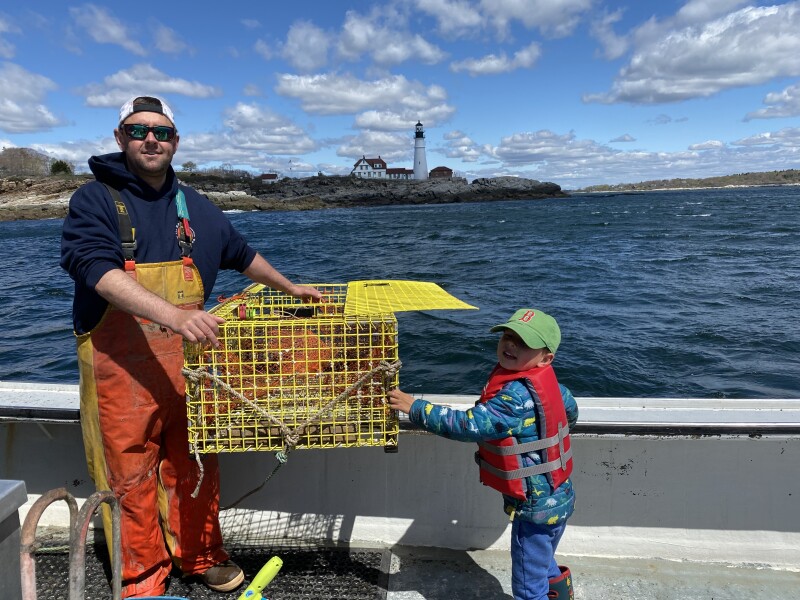 Curt Brown and his son, Finn, are holding a lobster trap in front of Portland Head Light—courtesy of the Brown family.