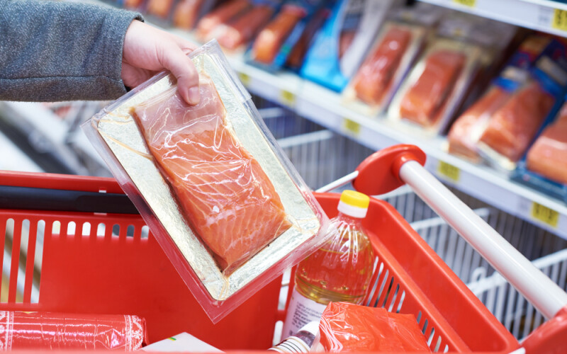 Grocery shopper putting packaged salmon into their cart.