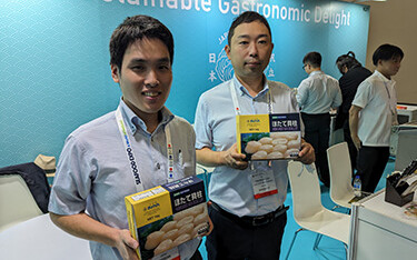 Two scallop producers from the Hokkaido prefecture of Japan posing with boxes of their product.