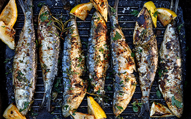 Sardines on a grill with lemon slices.
